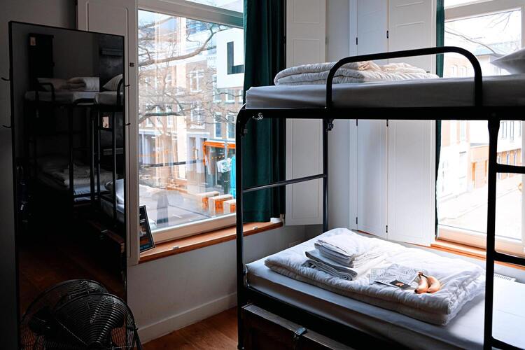 Une chambre avec des lits superposés et deux fenêtres donnant sur la rue