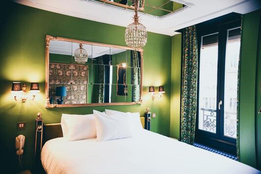 Une chambre verte avec lit double, plusieurs miroirs et une porte-fenêtre